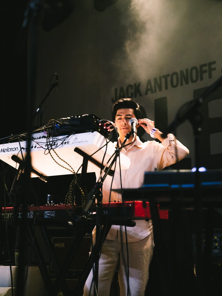 Taylor Heath stands onstage in front of a keyboard and audio equipment, adjusting his ear pieces.